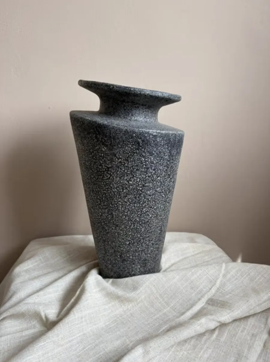 A plain phone photo of a ceramic vase on a bed
